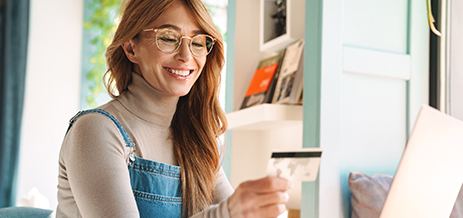 Woman working on computer, looking at debit card