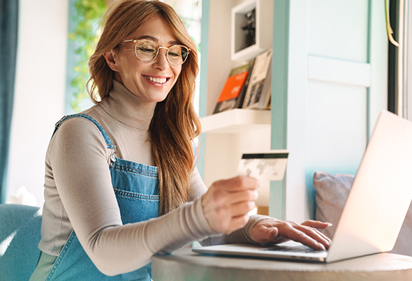 Woman using computer looking at debit card and smiling