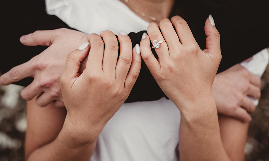 A woman with engagement ring holding man's arm.