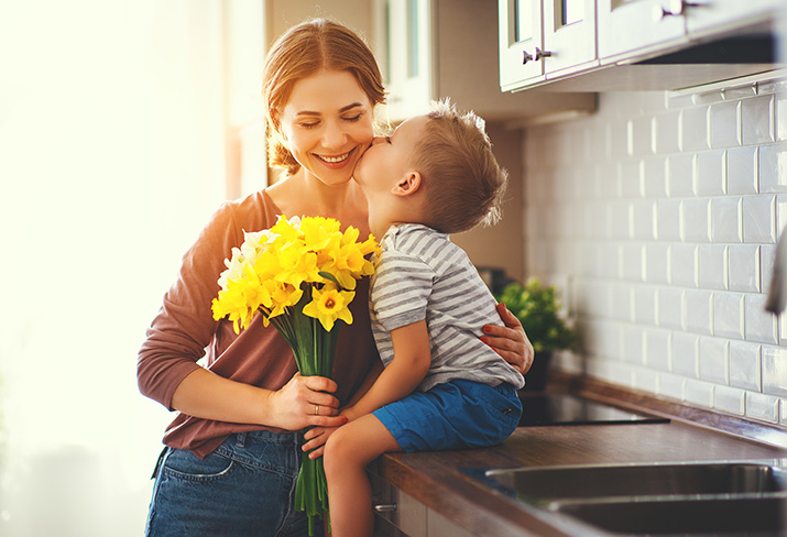 A mother holding flowers and hugging her son.